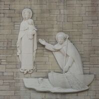 A stone relief of Our Lady holding the infant Jesus, with St Wilfrid in a boat on the sea, holding his crozier and reaching out towards the child