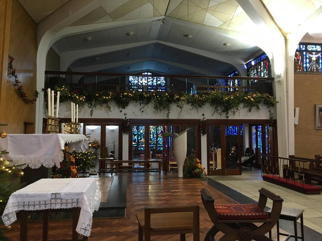 A view across the sanctuary at St Richard's, from the transept to the chapel, showing the church decorated for Christmas, with greenery and lights.