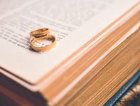 Two gold wedding rings lying on an open Latin Bible