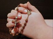 Hands folded in prayer, around a Rosary