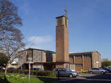 Photo of St Richard's Church, Chichester, a broad brick-built building with a brick bell tower, surmounted by a Cross.